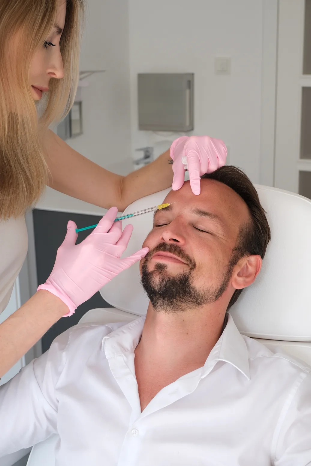 Dr. med. Lucija Grittern injiziert einem entspannten Mann mit rosa Handschuhen eine Behandlung in die Stirn.